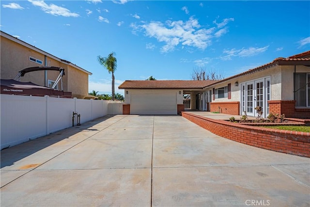 view of front of property with an attached garage, brick siding, fence, driveway, and french doors