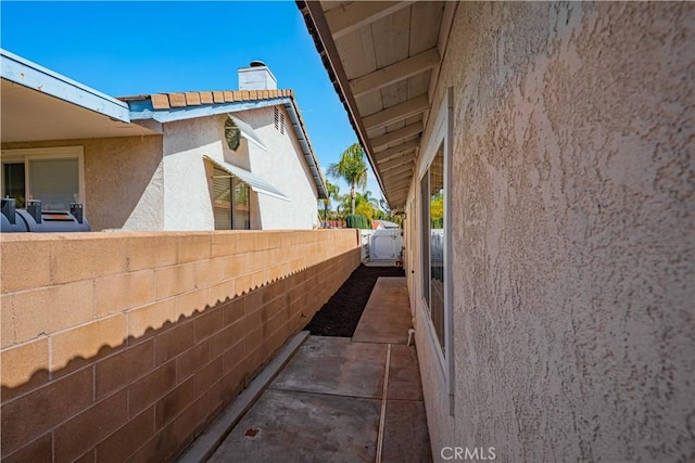 view of side of property with fence, a chimney, and stucco siding