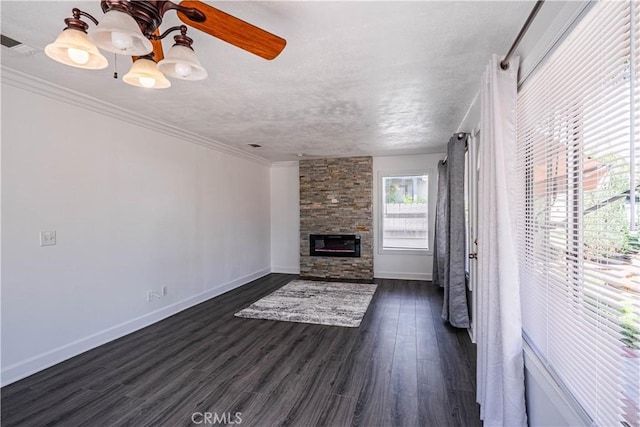 unfurnished living room with dark wood-style flooring, visible vents, ornamental molding, a stone fireplace, and baseboards