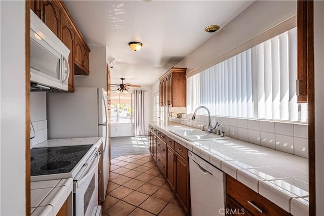 kitchen with tile countertops, backsplash, ceiling fan, a sink, and white appliances