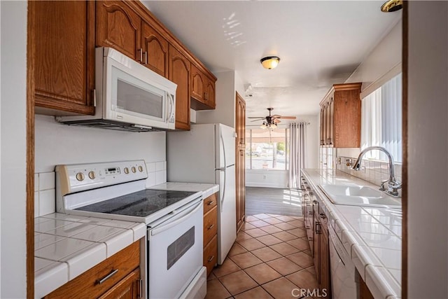 kitchen with white appliances, tile counters, brown cabinets, and a sink