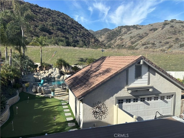 exterior space featuring a garage, a tile roof, a mountain view, and stucco siding