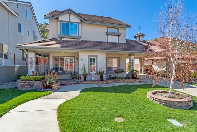 view of front of house with covered porch, a tiled roof, a front lawn, and stucco siding