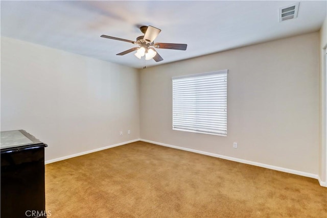 spare room with carpet floors, baseboards, visible vents, and a ceiling fan