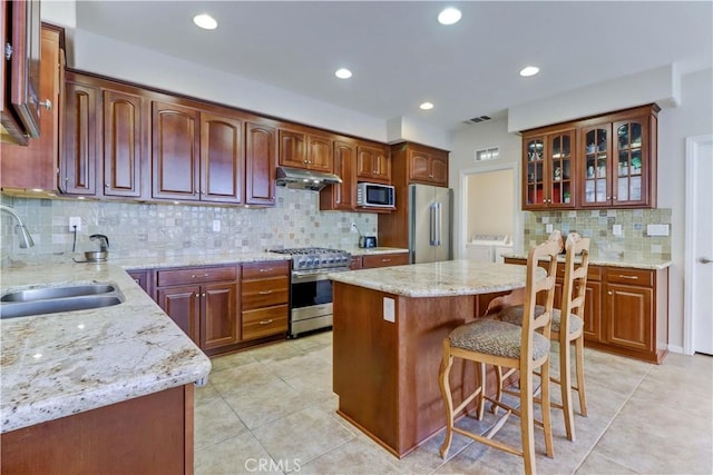 kitchen featuring visible vents, high end appliances, glass insert cabinets, under cabinet range hood, and a sink