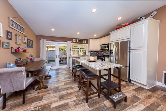 kitchen with white cabinets, appliances with stainless steel finishes, wood finished floors, light stone countertops, and french doors