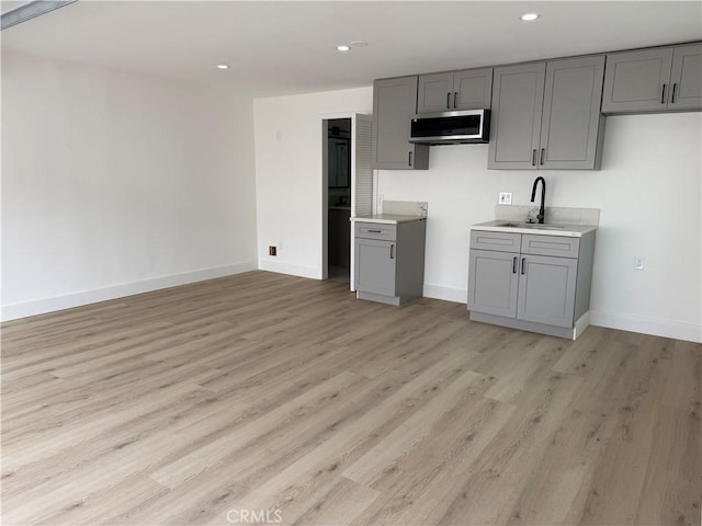 kitchen with light wood-style flooring, recessed lighting, a sink, gray cabinets, and stainless steel microwave