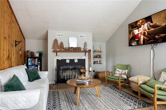 living area featuring visible vents, vaulted ceiling, and a glass covered fireplace