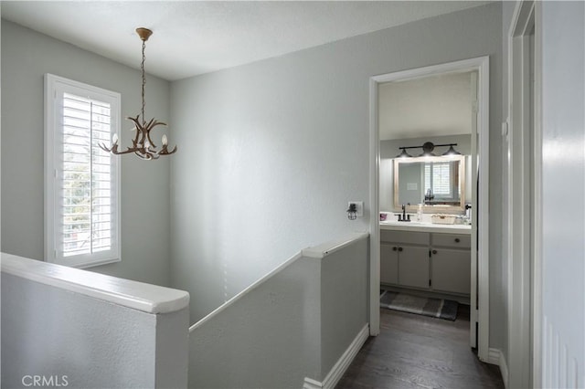 hallway with a sink, dark wood finished floors, an upstairs landing, and an inviting chandelier