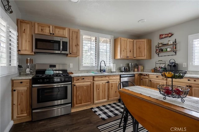 kitchen with light stone countertops, dark wood-style floors, appliances with stainless steel finishes, and a sink