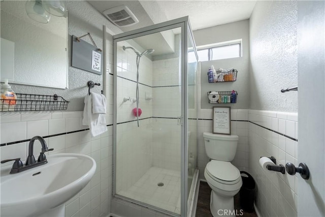 full bathroom featuring tile walls, visible vents, toilet, a stall shower, and a sink