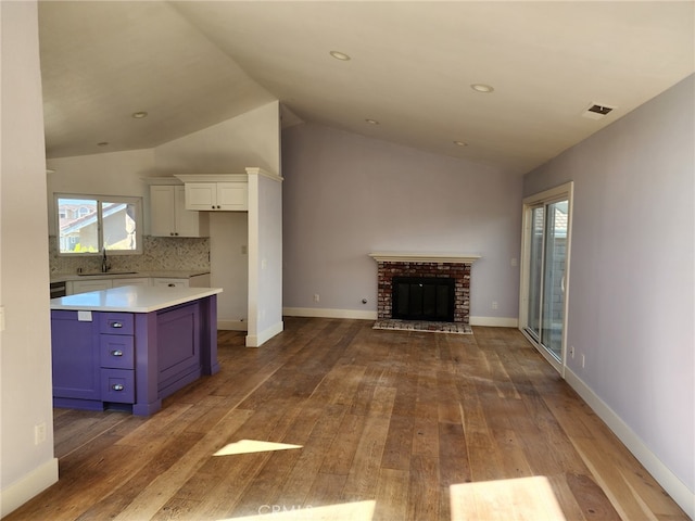 unfurnished living room featuring baseboards, hardwood / wood-style flooring, vaulted ceiling, a brick fireplace, and a sink