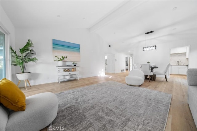 living room with light wood-style floors, visible vents, and vaulted ceiling with beams