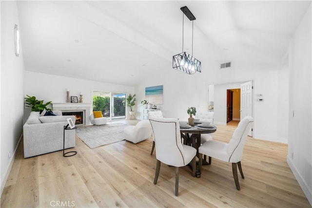 dining room featuring visible vents, an inviting chandelier, light wood-type flooring, a fireplace, and high vaulted ceiling