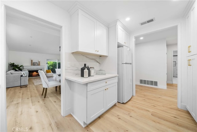 kitchen featuring freestanding refrigerator, a warm lit fireplace, visible vents, and white cabinetry