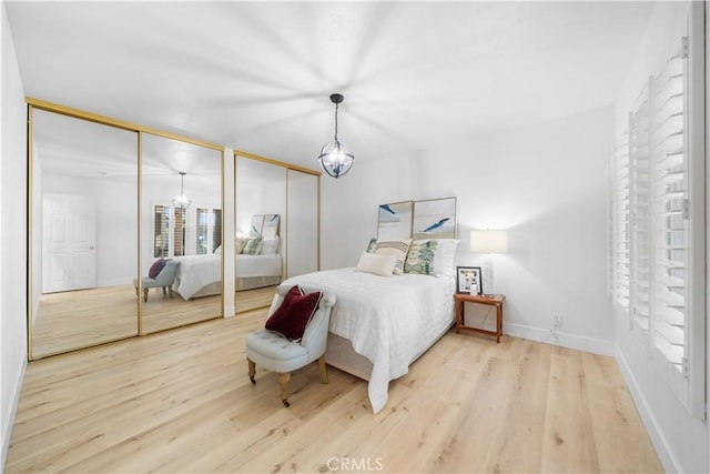 bedroom featuring baseboards, a chandelier, two closets, and wood finished floors