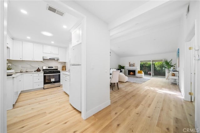 kitchen with a warm lit fireplace, visible vents, freestanding refrigerator, stainless steel gas range, and range hood