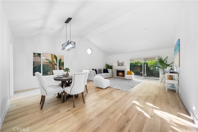 dining area with vaulted ceiling with beams, a lit fireplace, a chandelier, and light wood-style floors