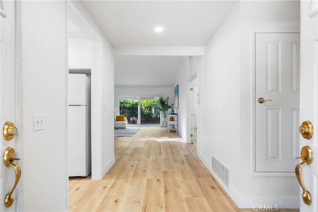 hall featuring baseboards, visible vents, and light wood finished floors