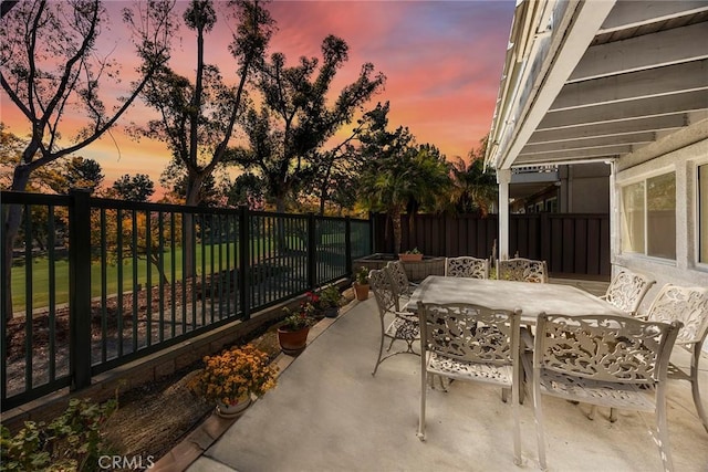 patio terrace at dusk featuring outdoor dining space and fence