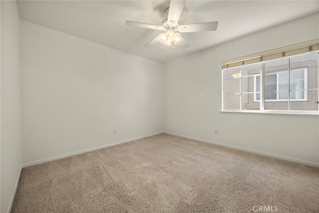 carpeted spare room featuring baseboards and a ceiling fan