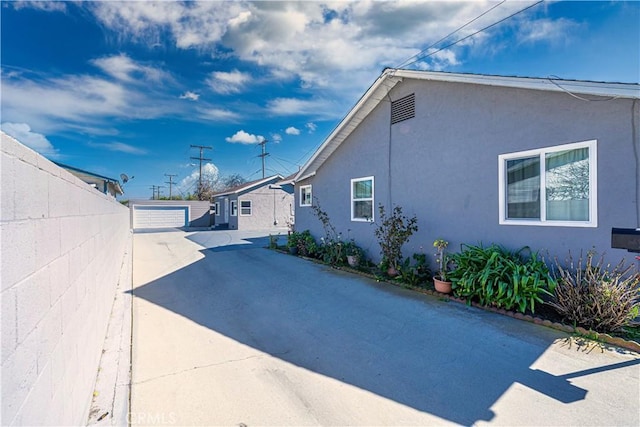 view of property exterior with fence, a detached garage, an outdoor structure, and stucco siding