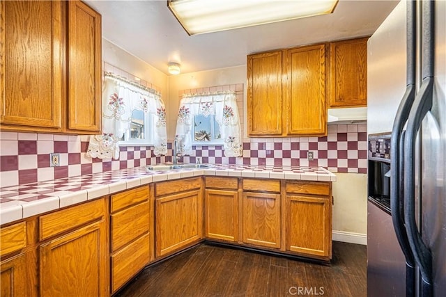 kitchen featuring a sink, backsplash, dark wood-style floors, brown cabinetry, and stainless steel fridge