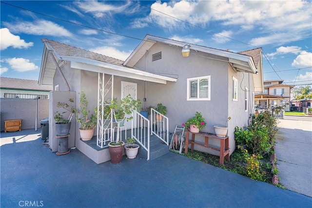 view of front of home with a patio area, roof with shingles, fence, and stucco siding