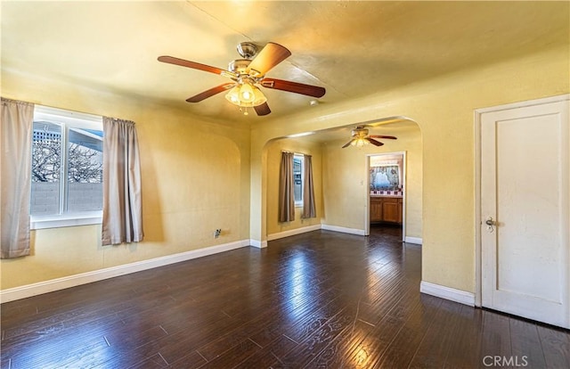 spare room featuring baseboards, arched walkways, dark wood finished floors, and a ceiling fan