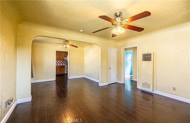 unfurnished room featuring arched walkways, dark wood-style flooring, visible vents, and baseboards