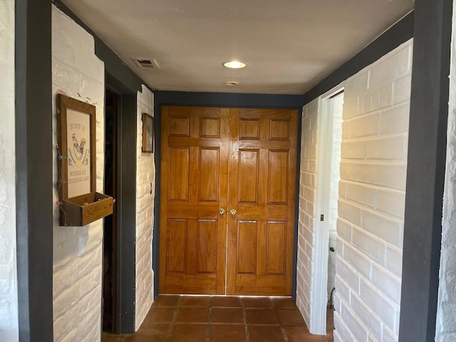 hall with visible vents, dark tile patterned flooring, and brick wall