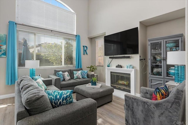 living area with a glass covered fireplace, plenty of natural light, baseboards, and wood finished floors