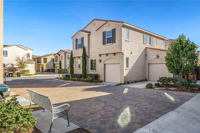 mediterranean / spanish home with decorative driveway, a tile roof, stucco siding, a garage, and a residential view