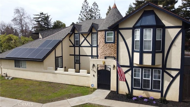 tudor house featuring a fenced front yard, roof with shingles, a gate, and stucco siding