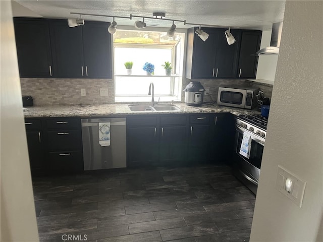 kitchen with tasteful backsplash, appliances with stainless steel finishes, dark cabinets, wall chimney range hood, and a sink