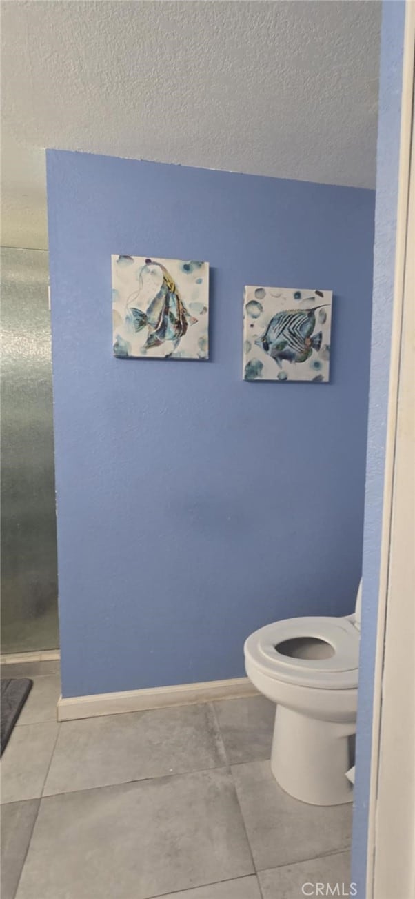 bathroom featuring toilet, tile patterned flooring, baseboards, and a textured ceiling