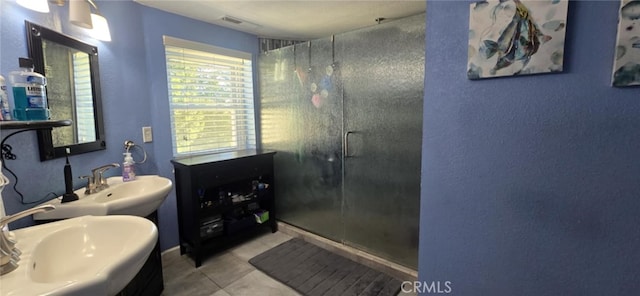 bathroom with a stall shower, two sinks, visible vents, and tile patterned floors