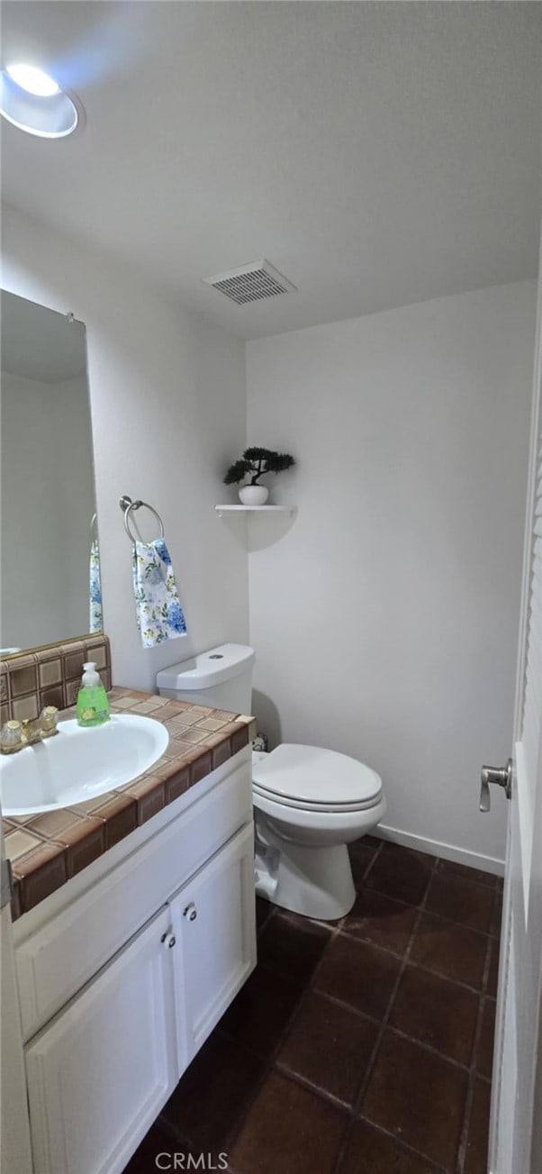 bathroom featuring tile patterned flooring, toilet, vanity, visible vents, and baseboards