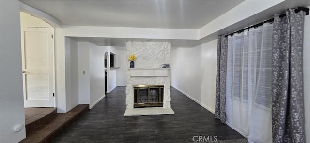 unfurnished living room with arched walkways, a stone fireplace, baseboards, and wood finished floors