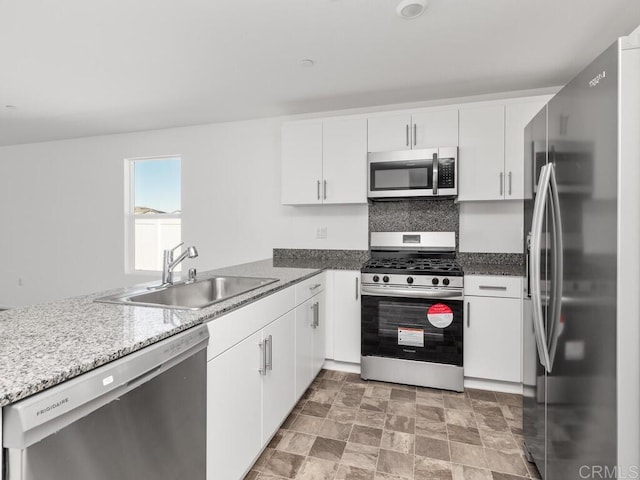 kitchen featuring white cabinets, stone finish floor, stainless steel appliances, and a sink