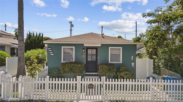 bungalow-style home with a fenced front yard, a shingled roof, and stucco siding