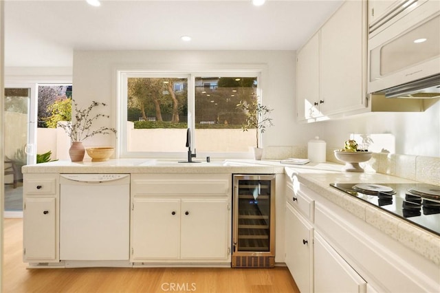 kitchen with white appliances, wine cooler, light countertops, light wood-type flooring, and a sink