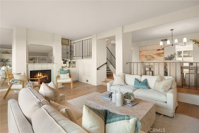 living room featuring visible vents, wood finished floors, a high end fireplace, stairway, and a chandelier