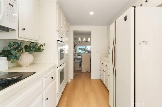 kitchen with light wood-type flooring, light countertops, white appliances, and white cabinets