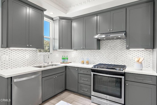 kitchen featuring under cabinet range hood, stainless steel appliances, a sink, light countertops, and gray cabinets