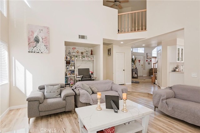 living area with visible vents, baseboards, a towering ceiling, light wood-style flooring, and ceiling fan