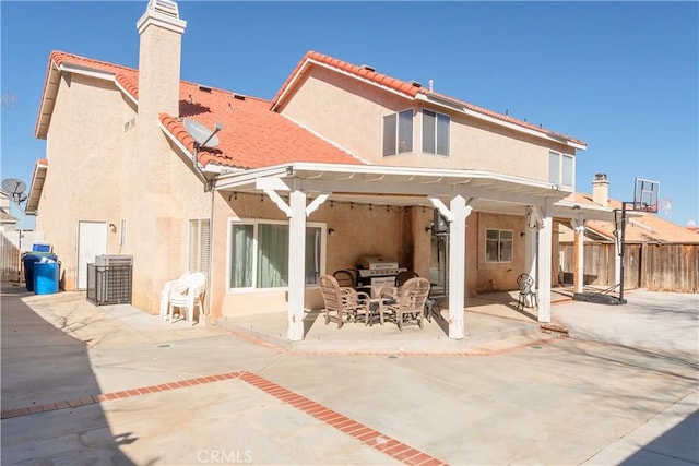 back of property with a patio, a chimney, stucco siding, fence, and a tiled roof