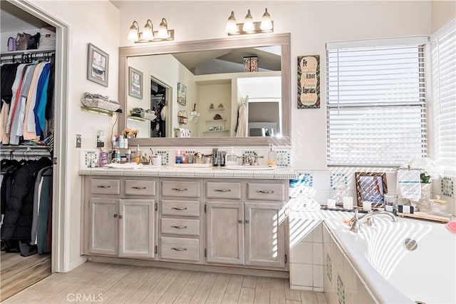 bathroom featuring double vanity, a garden tub, and a walk in closet