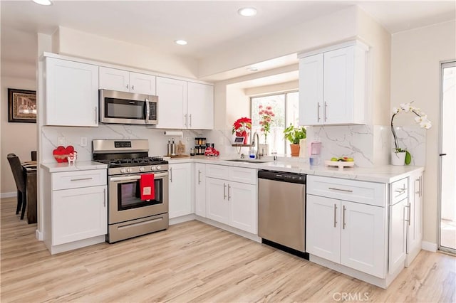 kitchen featuring light wood finished floors, stainless steel appliances, light countertops, white cabinets, and a sink