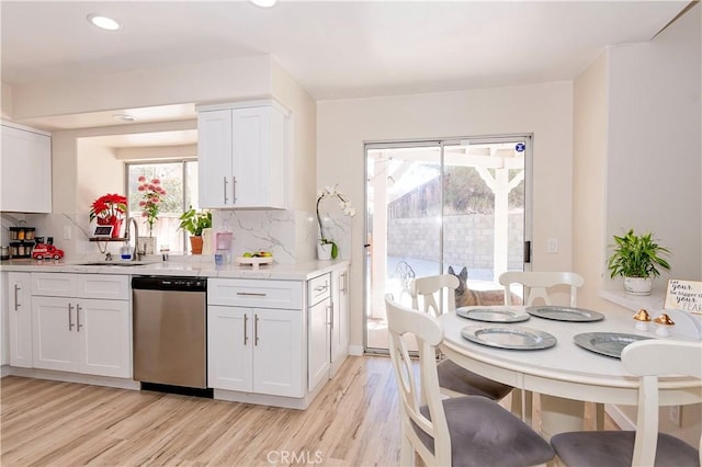 kitchen featuring light wood finished floors, backsplash, white cabinetry, a sink, and dishwasher